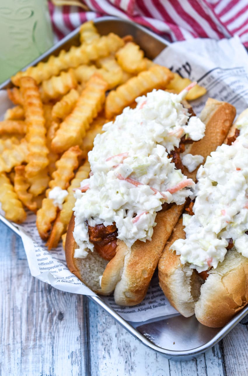 two carolina slaw dogs on a news paper lined metal serving tray with crinkle cut french fries on the side