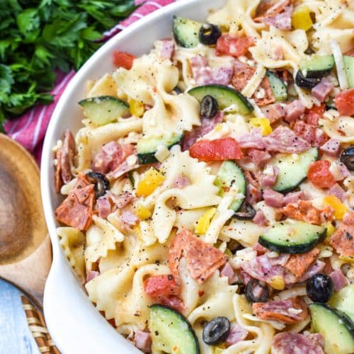 Italian pasta salad in a white serving bowl with a wooden spoon on the side
