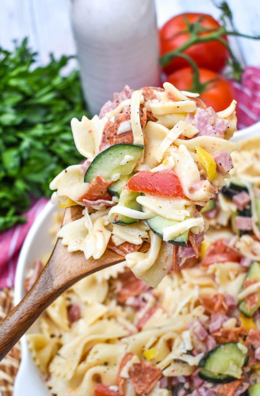 a wooden spoon holding up a scoop of italian pasta salad