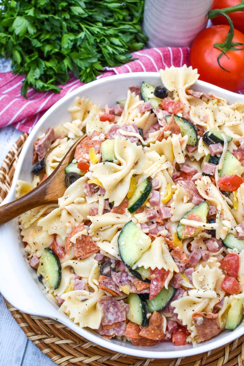 a wooden spoon resting in a white bowl filled with italian pasta salad