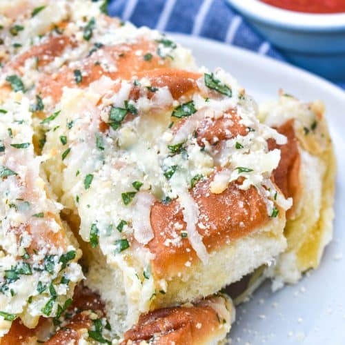 a pile of cheesy hawaiian roll garlic bread on a small white plate with a bowl of marinara on the side