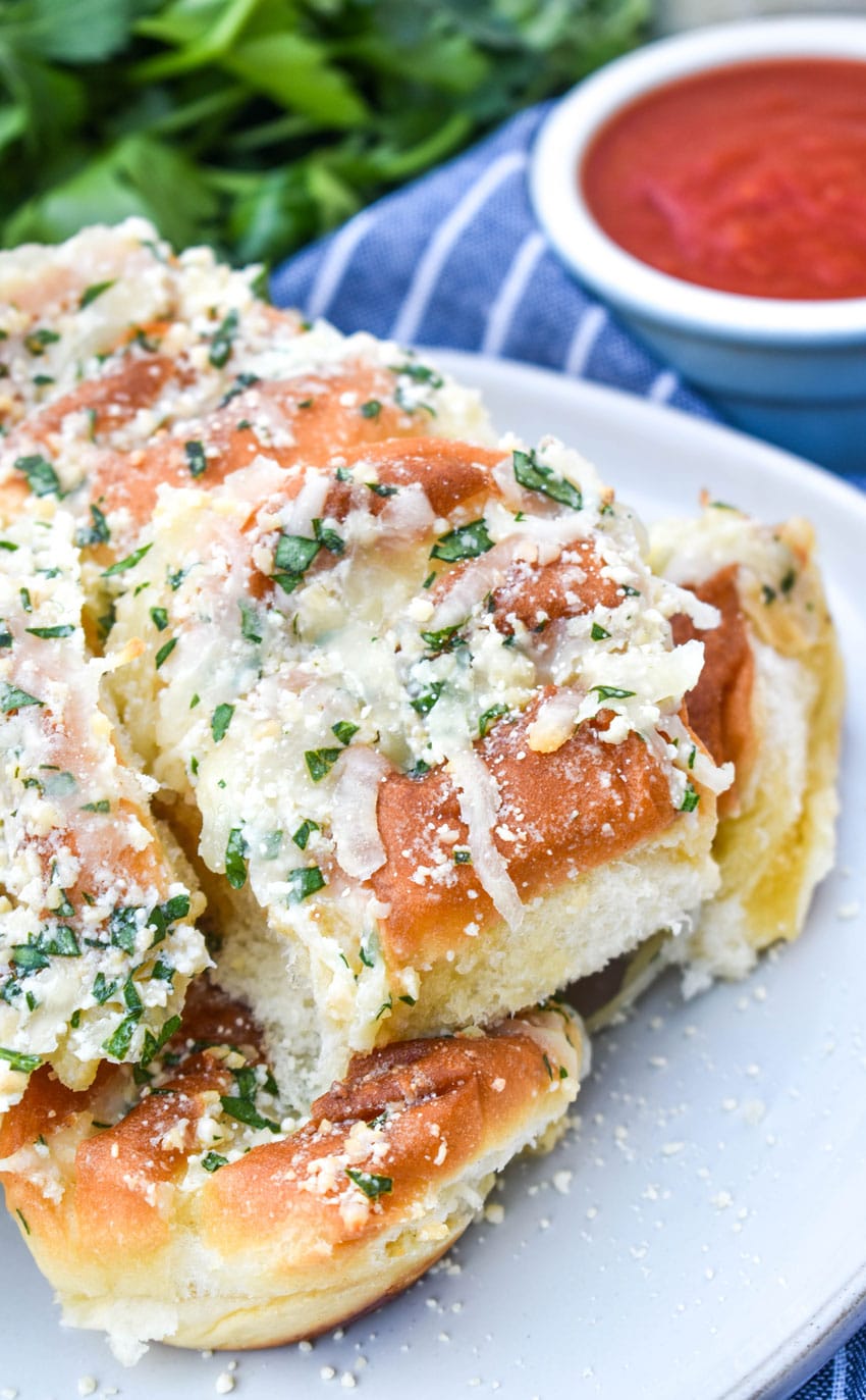 a pile of cheesy hawaiian roll garlic bread on a small white plate with a bowl of marinara on the side
