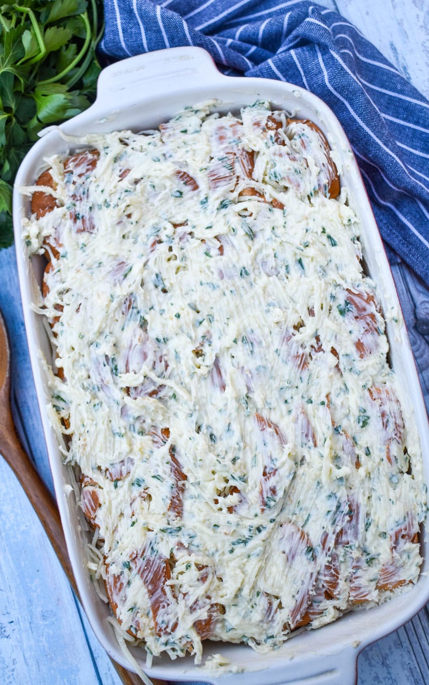 garlic butter and shredded cheese spread evenly out over hawaiian rolls in a white baking dish