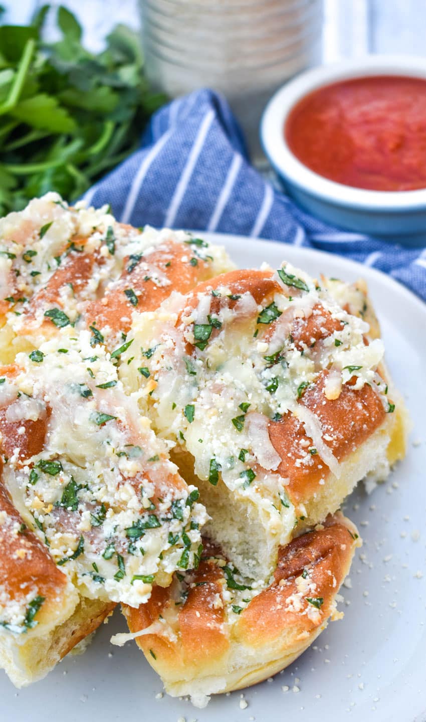 a pile of cheesy hawaiian roll garlic bread on a small white plate with a bowl of marinara on the side