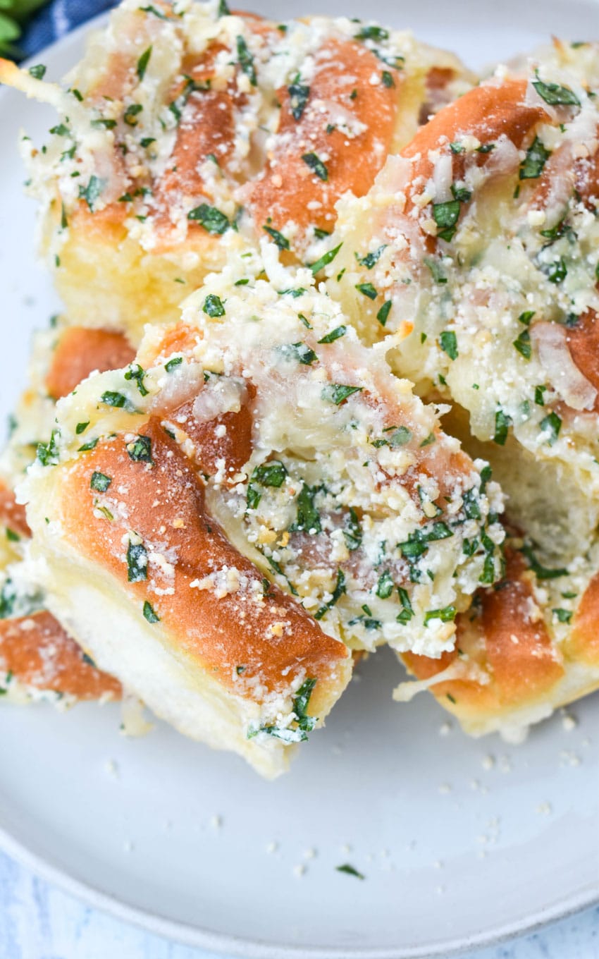 a pile of cheesy hawaiian roll garlic bread on a small white plate with a bowl of marinara on the side