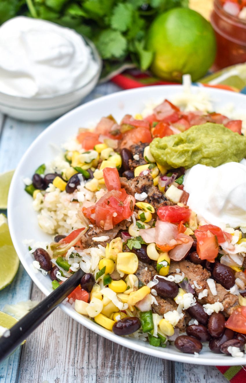 a black fork scooping copycat chipotle burrito bowls out of a shallow white serving dish