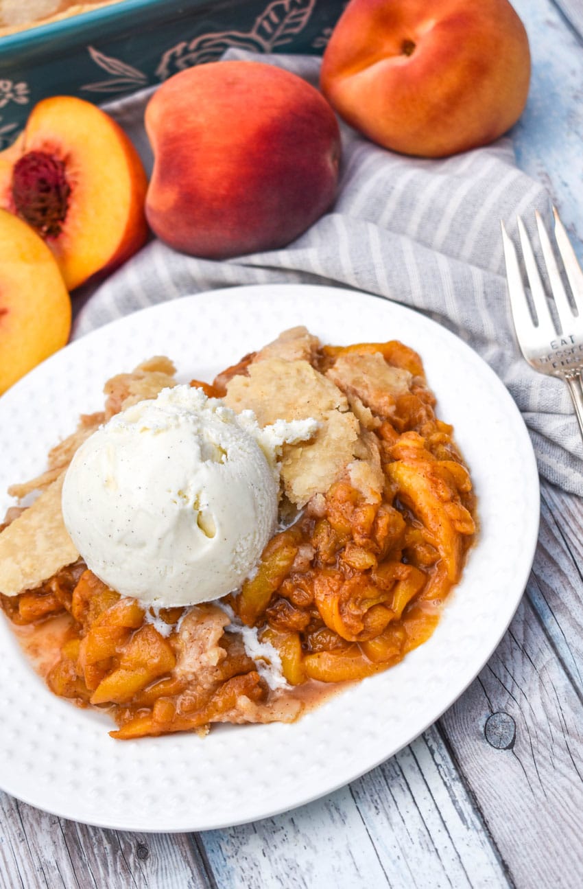 easy homemade peach cobbler on a white plate topped with a scoop of melting vanilla ice cream