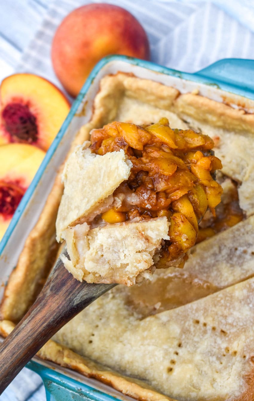 a wooden spoon holding up a scoop of easy homemade peach cobbler