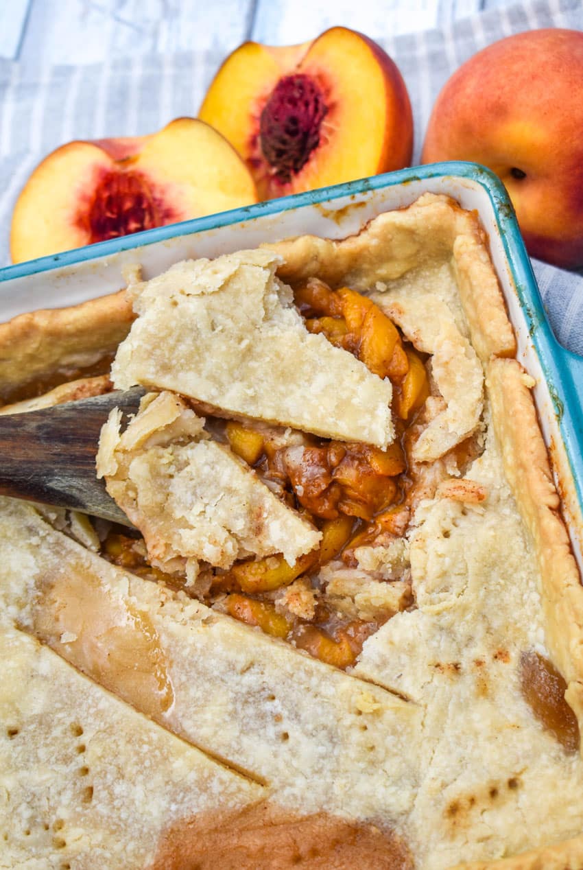 a wooden spoon scooping southern peach cobbler out of a small blue baking dish