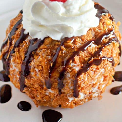 fried ice cream topped with a drizzle of chocolate sauce, whipped cream, and a a maraschino cherry on a small white plate