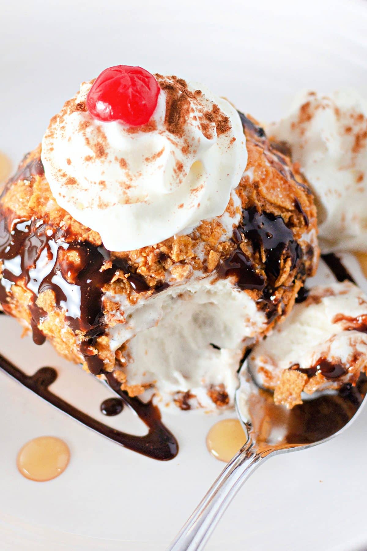 fried ice cream topped with a drizzle of chocolate sauce, whipped cream, and a a maraschino cherry on a small white plate