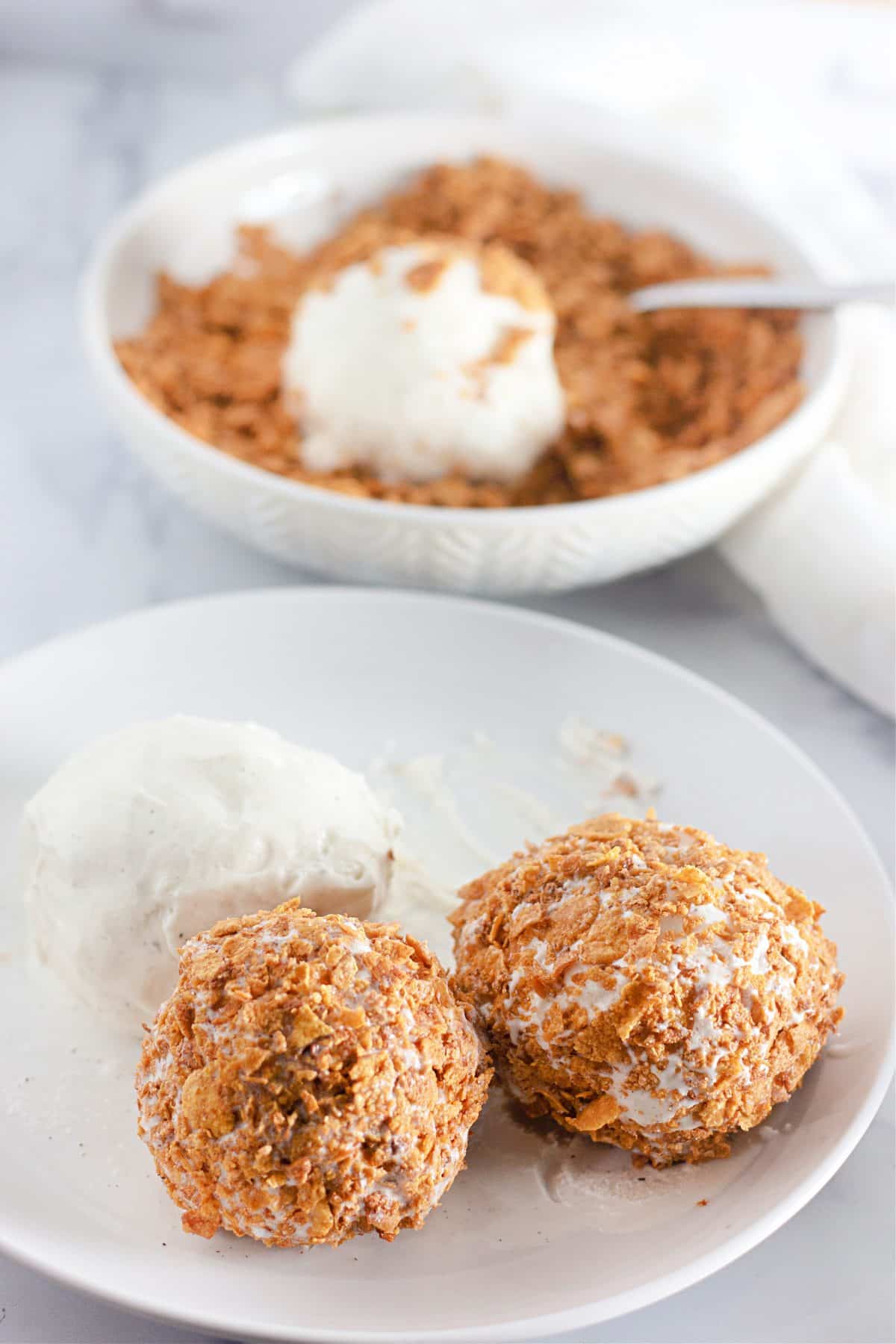 three ice cream balls on  a white plate, two of which have been coated in cornflakes cereal