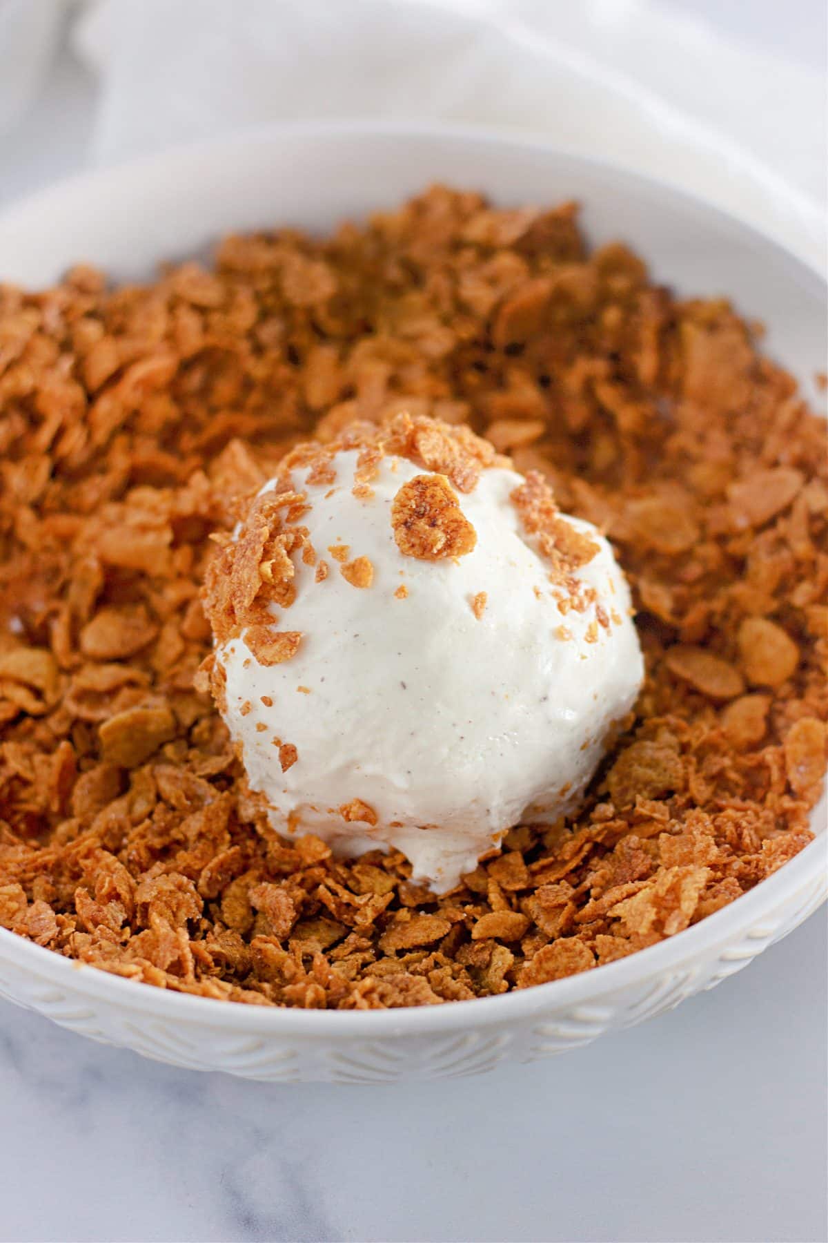 a ball of vanilla ice cream sitting in a bowl of toasted cornflakes cereal