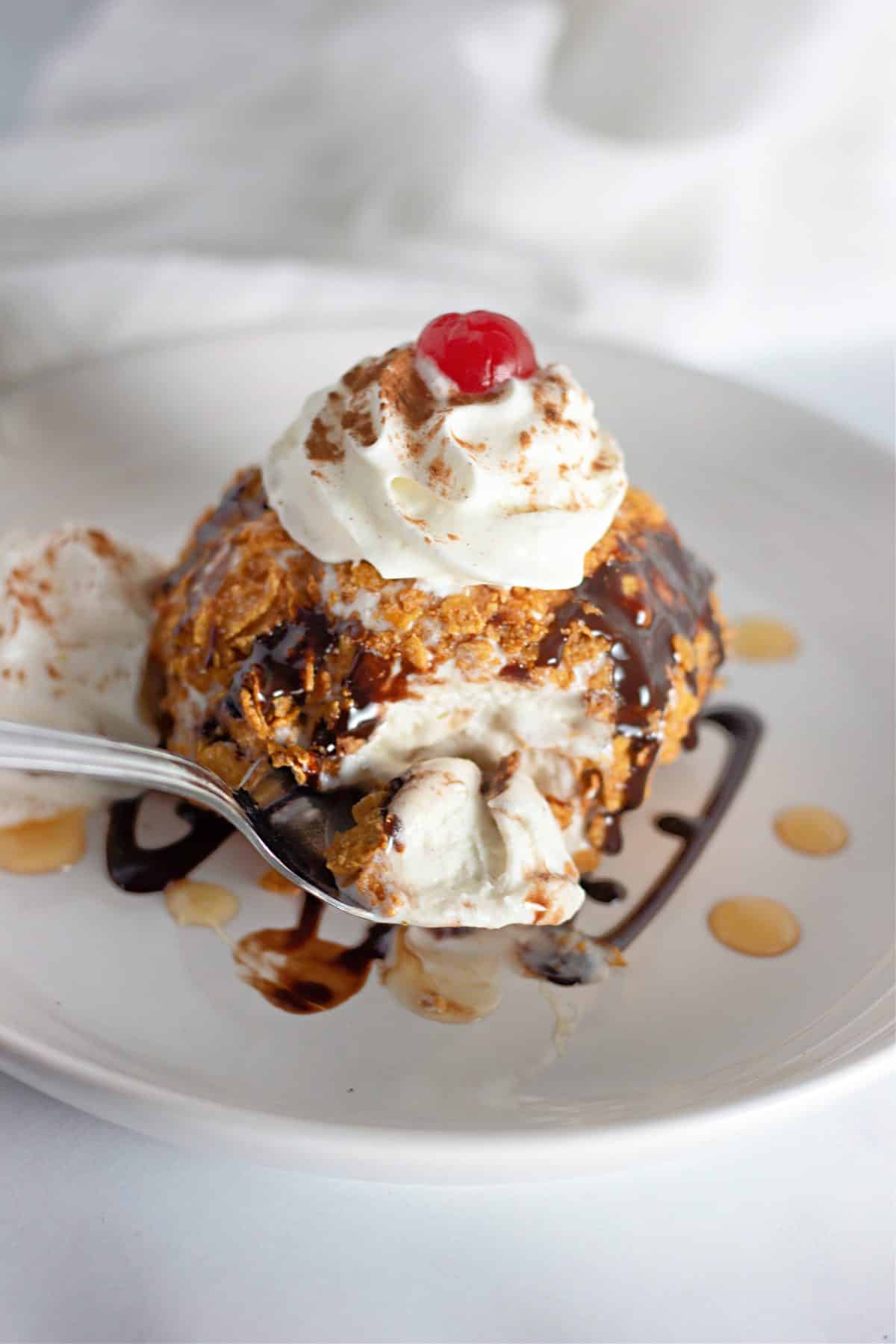a silver spoon scooping fried ice cream off a small white plate