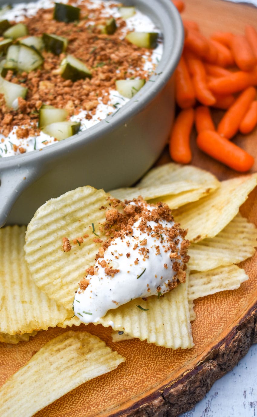 a pile of chips on a wooden cutting board with a dollop of southern fried pickle dip on top