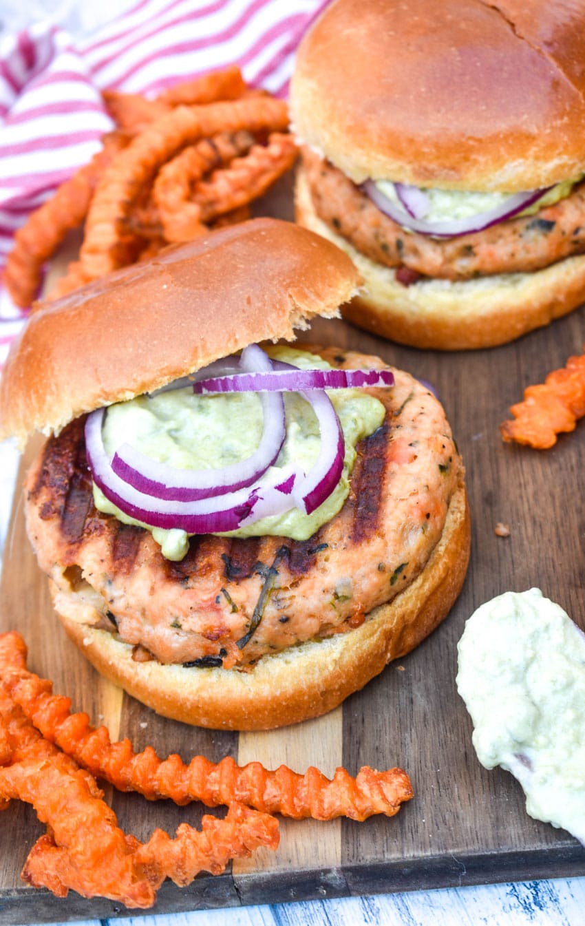 spinach feta salmon burgers on a wooden cutting board with sweet potato fries on the side