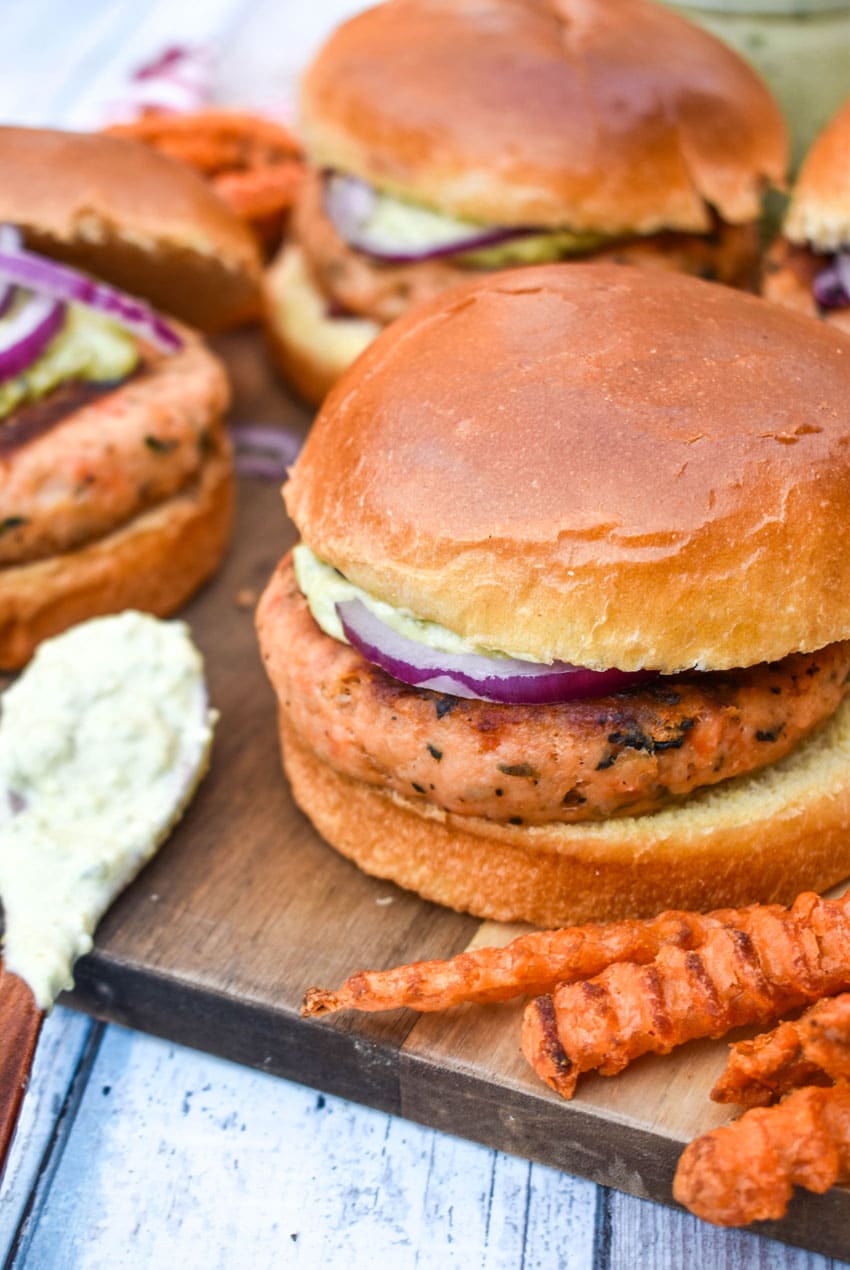 spinach feta salmon burgers on a wooden cutting board with sweet potato fries on the side
