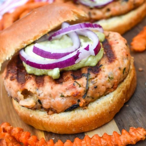 spinach feta salmon burgers on a wooden cutting board with sweet potato fries on the side