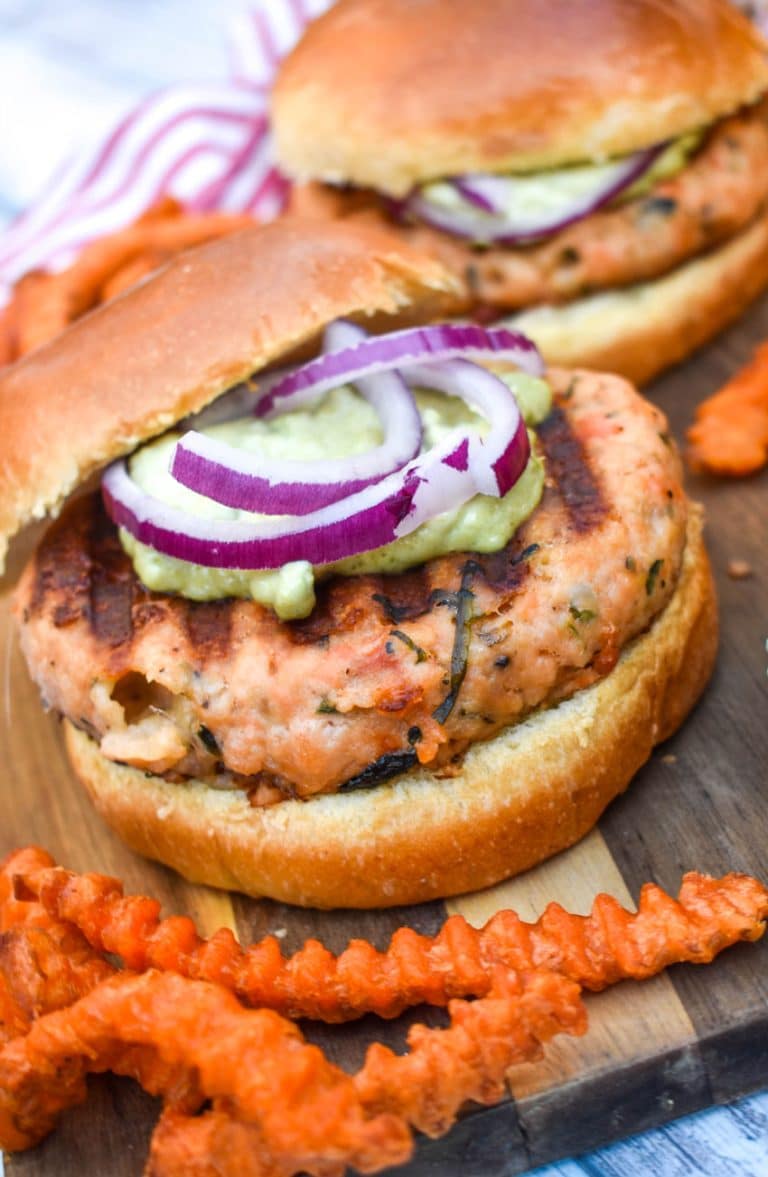 spinach feta salmon burgers on a wooden cutting board with sweet potato fries on the side