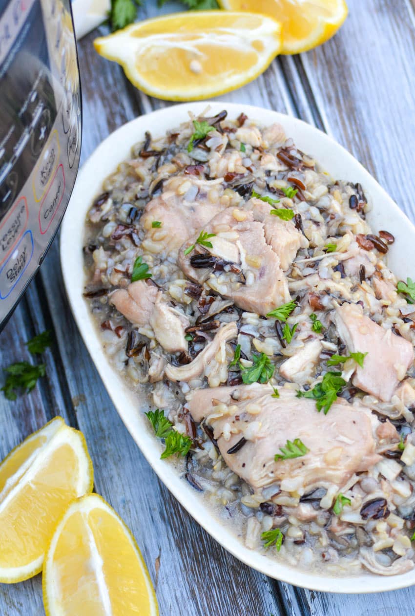 lemon chicken and wild rice in a small serving bowl with lemon wedges on the side and an instant pot in the background