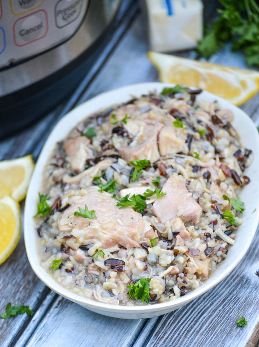 lemon chicken and wild rice topped with fresh herbs in a small serving bowl with lemon wedges on the side and an instant pot in the background