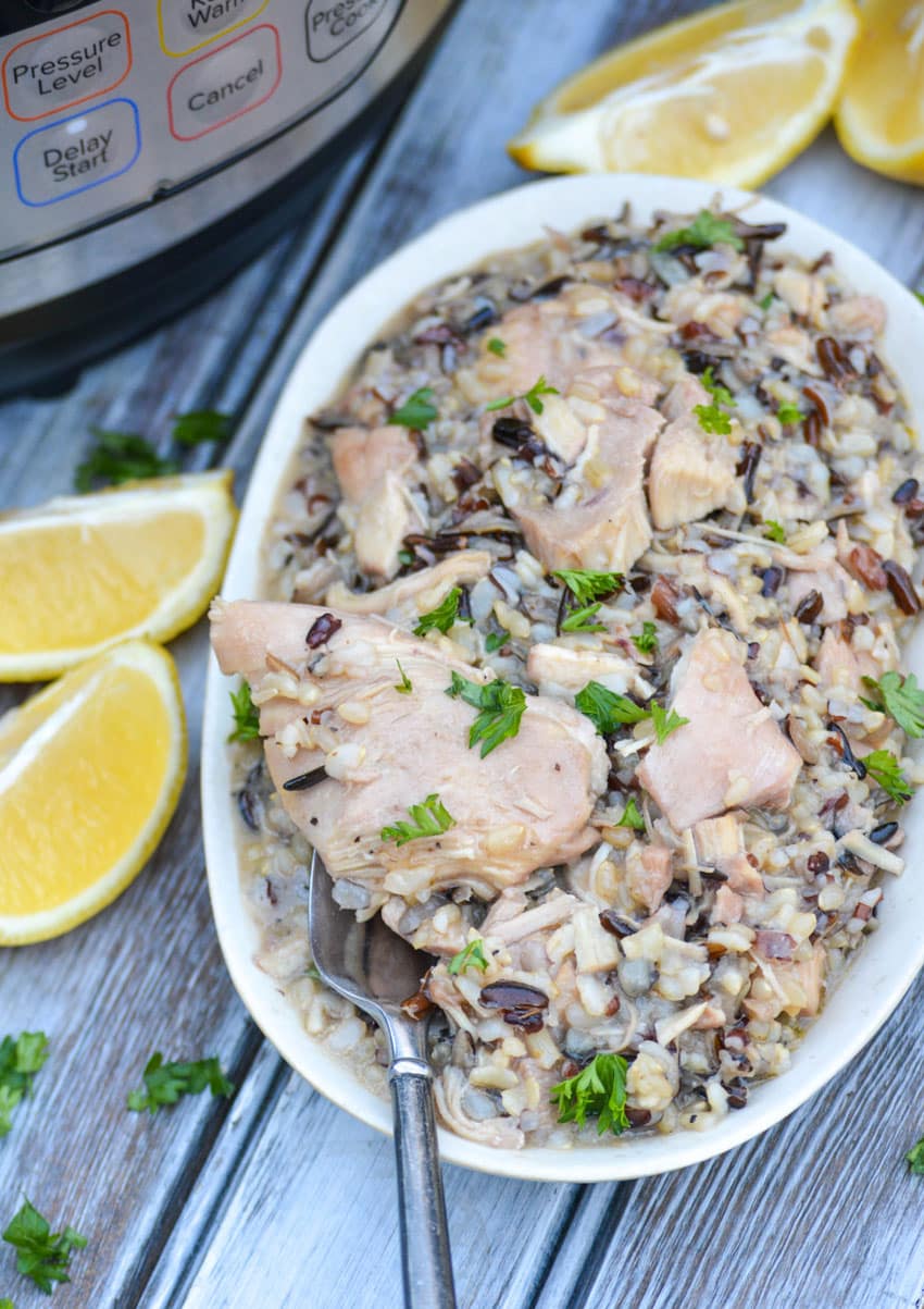 a silver fork scooping instant pot lemon chicken and wild rice out of a small serving bowl with lemon wedges on the sides