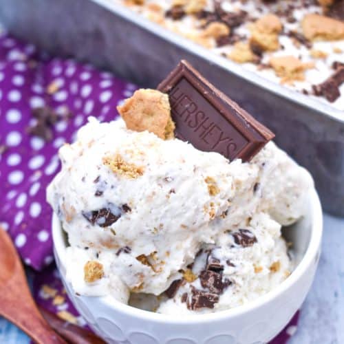 no churn s'mores ice cream in a small white bowl with a piece of graham cracker and chocolate square stuck on top and wooden spoons on the side