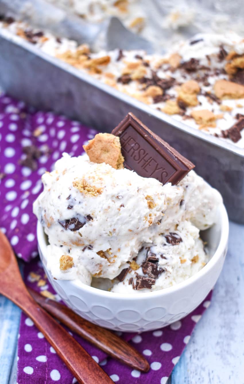 S'mores Ice Cream (No Churn Recipe) no churn s'mores ice cream in a small white bowl with a piece of graham cracker and chocolate square stuck on top and wooden spoons on the side