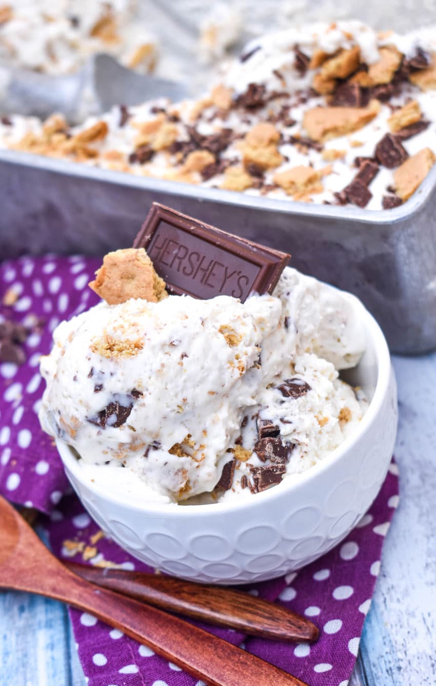 no churn s'mores ice cream in a small white bowl with a piece of graham cracker and chocolate square stuck on top and wooden spoons on the side