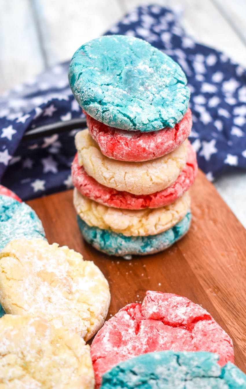 a stack of red white and blue cake mix cookies on the edge of a wooden cutting board