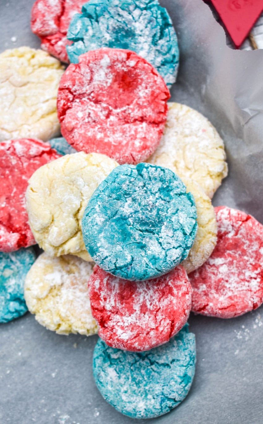 Red White & Blue Crinkle Cookies red white and blue crinkle cookies in a pile in the corner of a parchment paper lined baking sheet