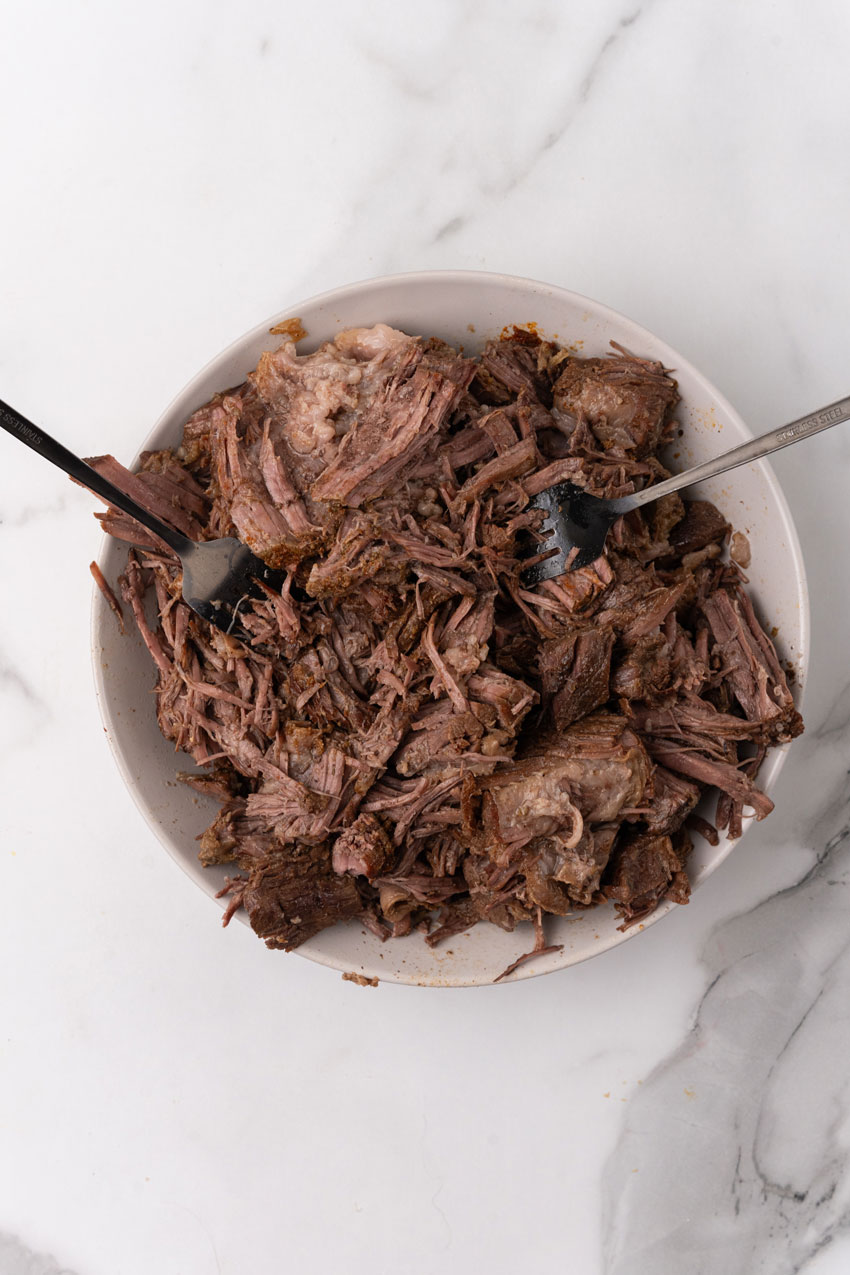 shredded beef on a white plate with two forks resting on the side