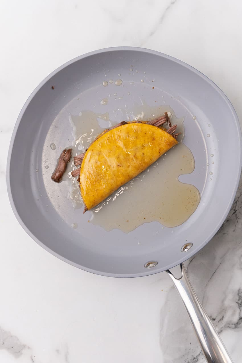 a quesa birria taco in oil in a large skillet