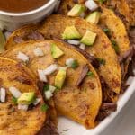 instant pot birria tacos topped with avocado pieces and diced white onion arranged in a row on a white serving platter