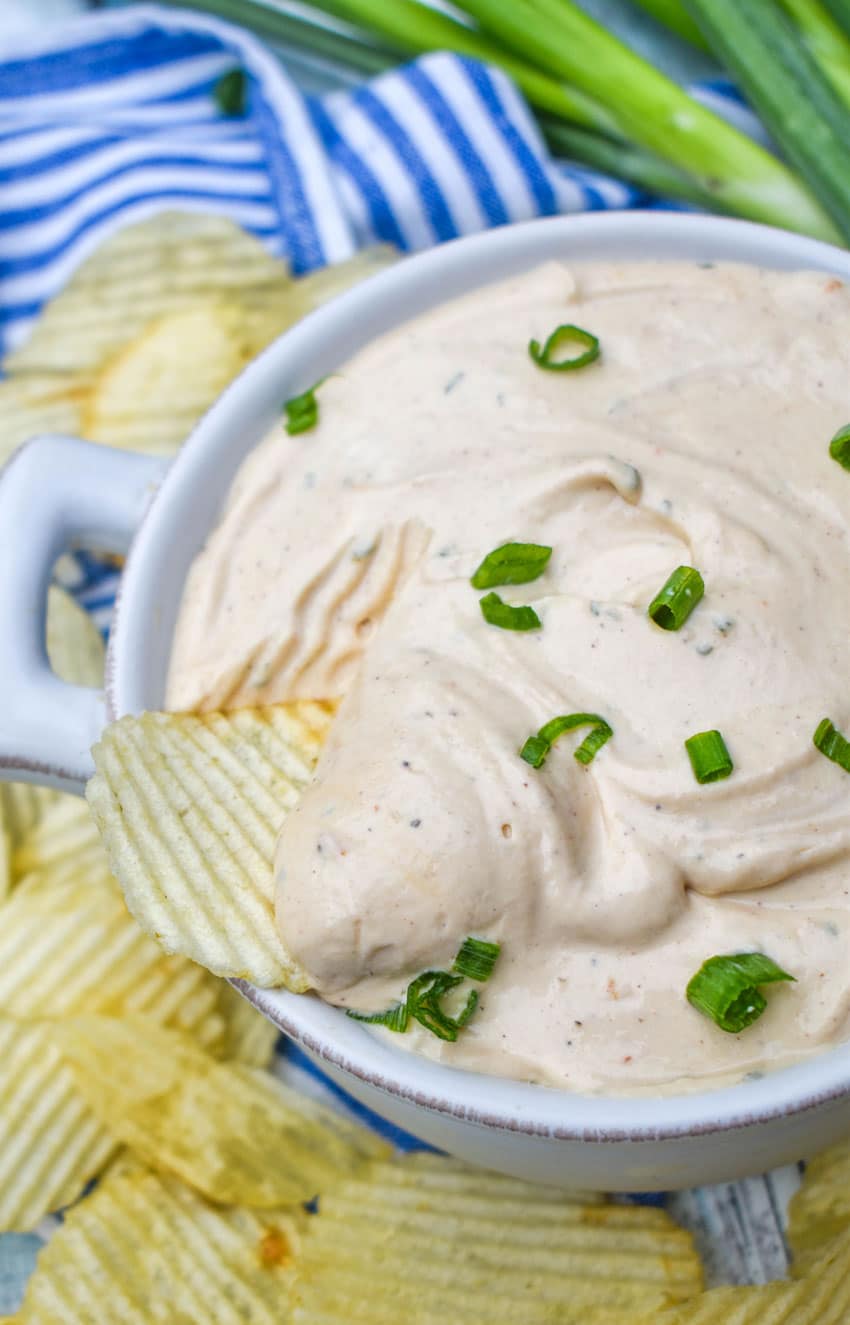 a potato chip scooping barbecue sour cream out of a small white bowl