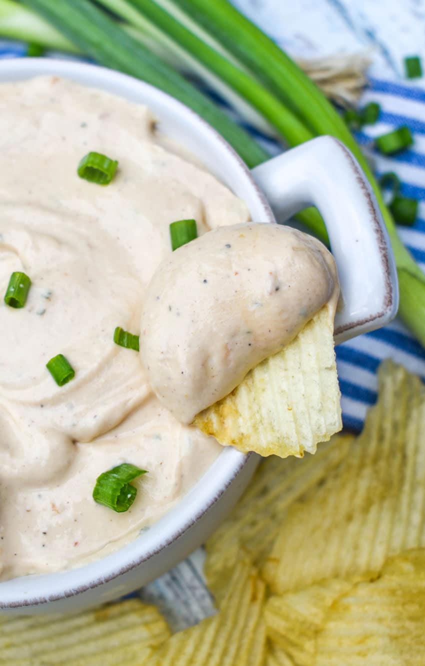 a potato chip scooping barbecue sour cream out of a small white bowl