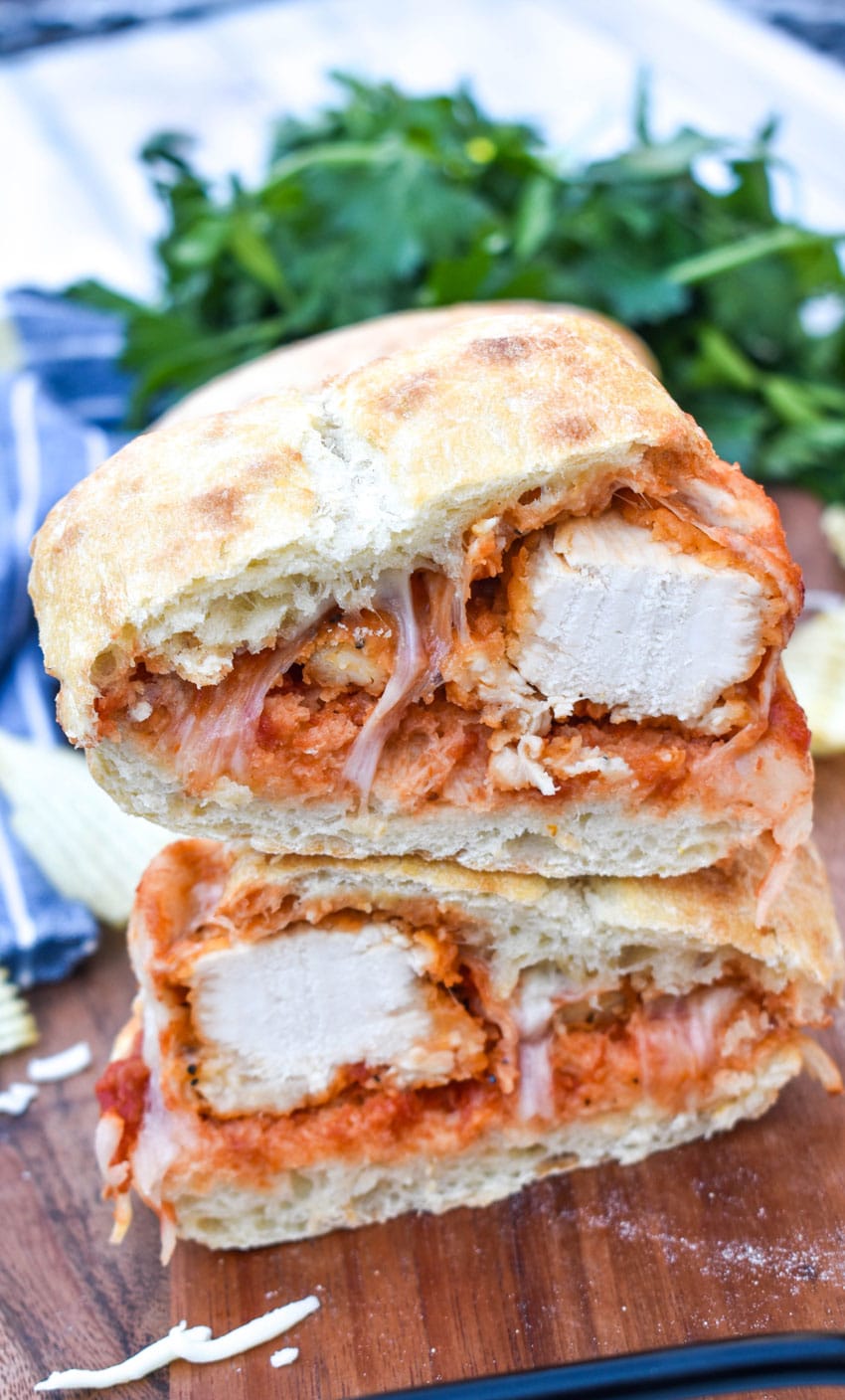 two slices of air fried chicken parmesan cheese sandwiches stacked together on a wooden cutting board