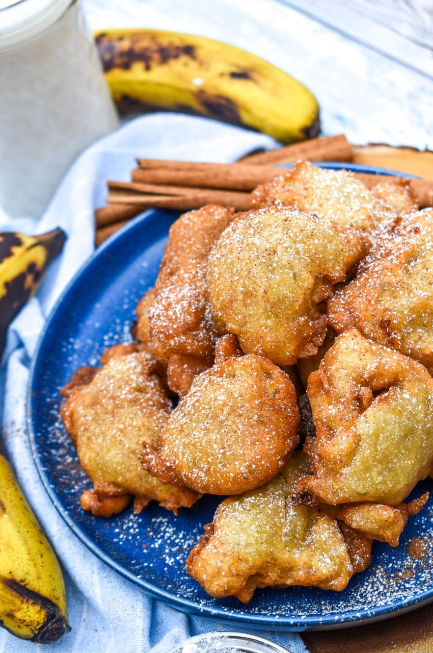a pile of fried banana fritters sprinkled with powdered sugar on a blue plate