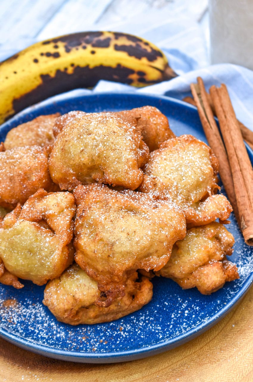 a pile of fried banana fritters sprinkled with powdered sugar on a blue plate