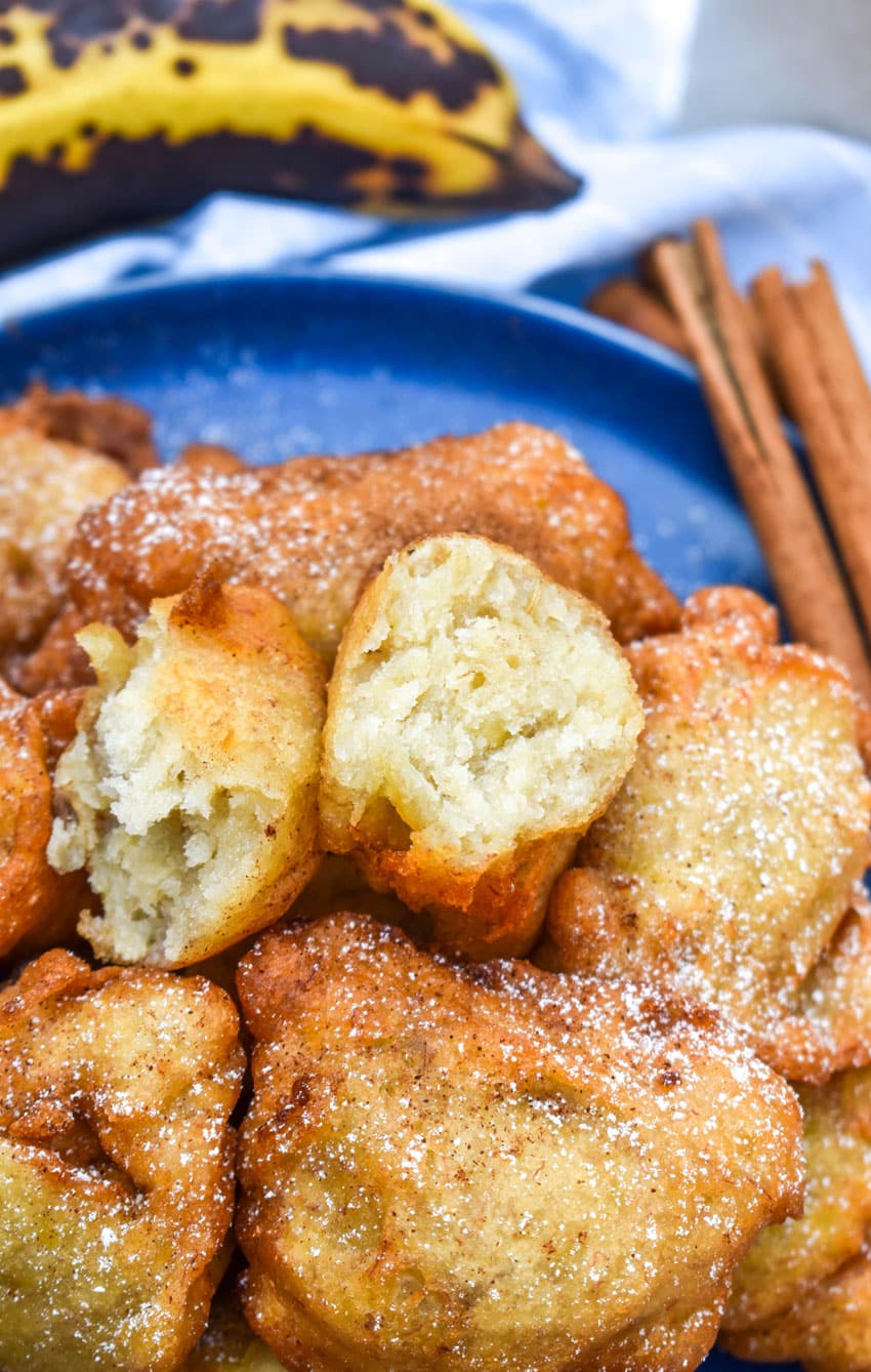 a fried banana fritter sliced in half resting on a pile of fritters on a blue plate