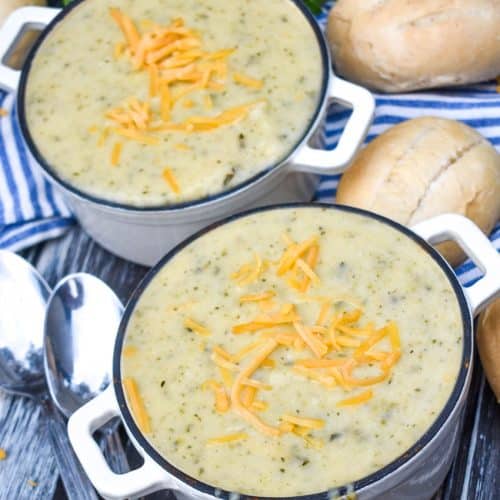 creamy zucchini soup topped with melting shreds of cheddar cheese in two small white cast iron bowls