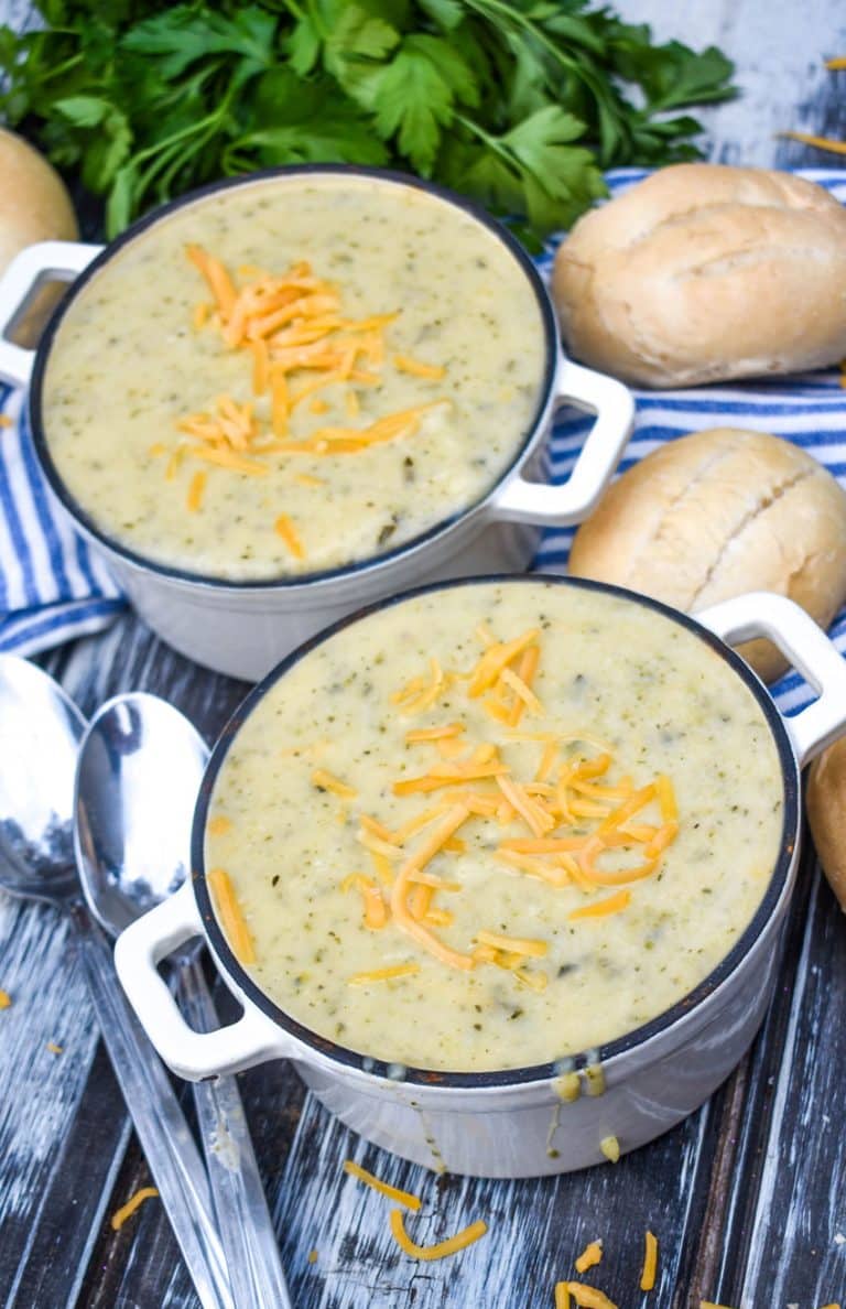 creamy zucchini soup topped with melting shreds of cheddar cheese in two small white cast iron bowls