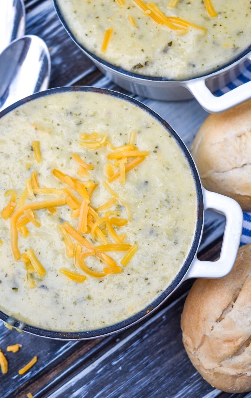 creamy zucchini soup topped with melting shreds of cheddar cheese in two small white cast iron bowls