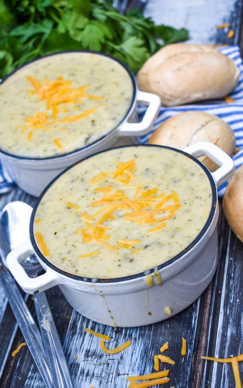 creamy zucchini soup topped with melting shreds of cheddar cheese in two small white cast iron bowls