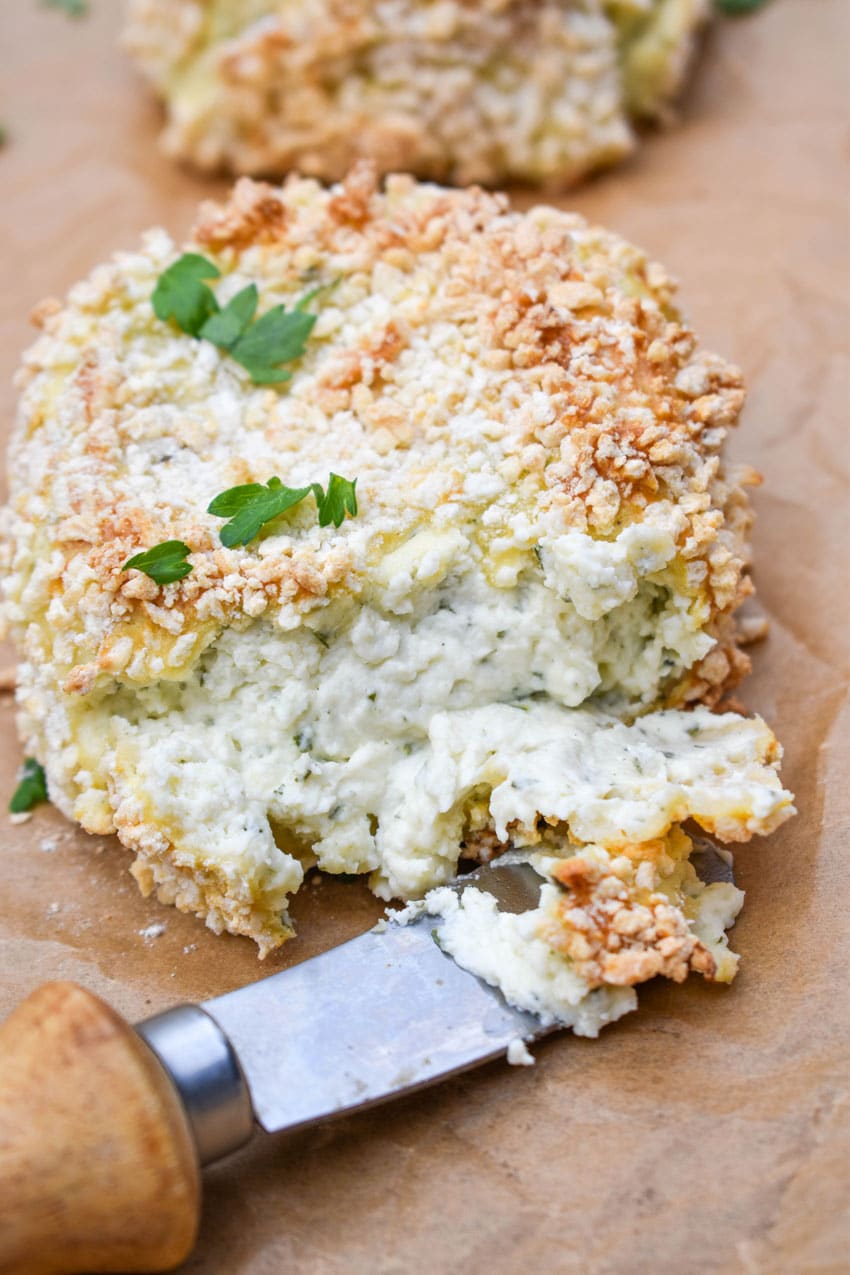 A CHEESE SPREADER CUTTING INTO CRISPY BAKED BOURSIN CHEESE