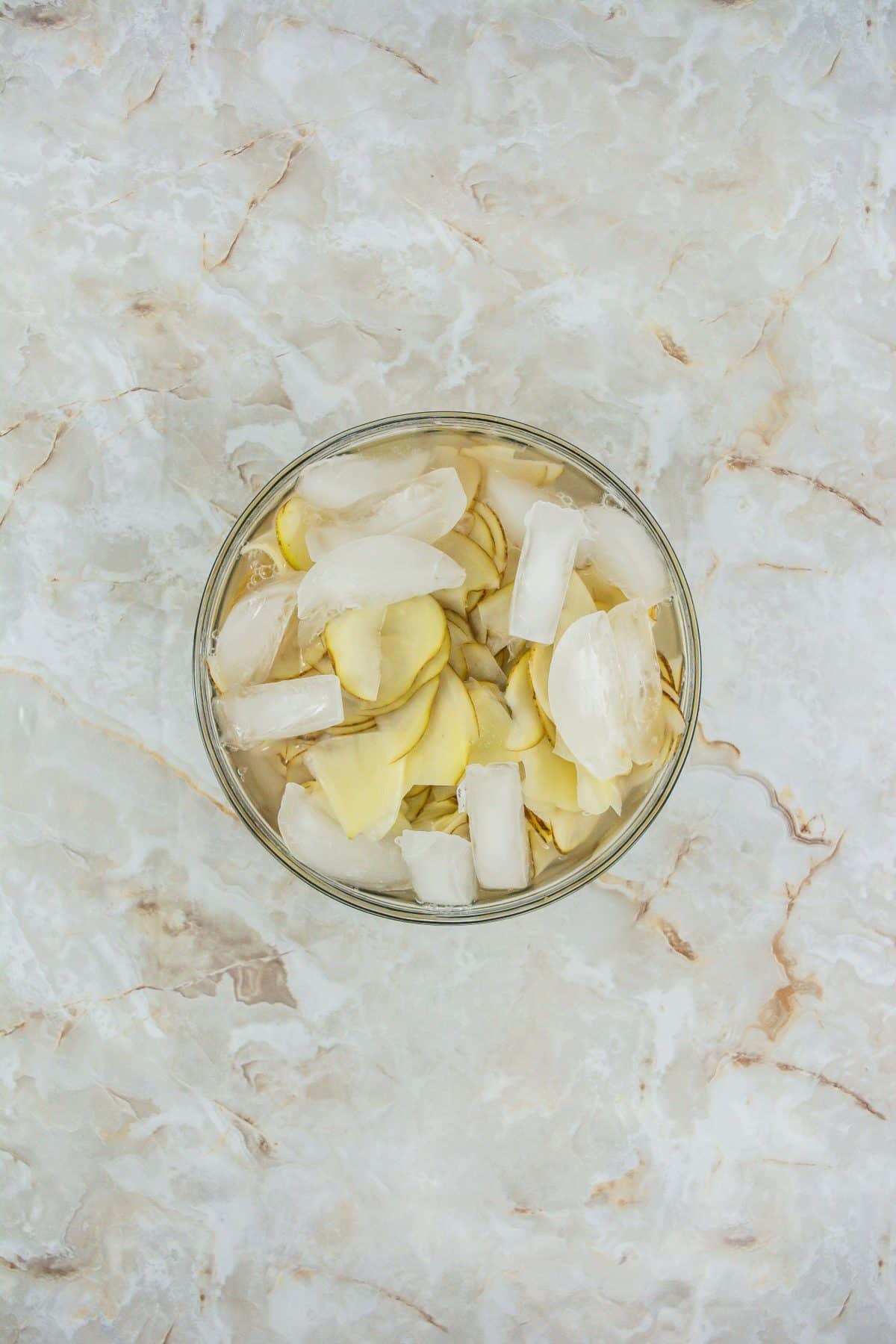 slices of russet potatoes in an ice water bath in a glass bowl