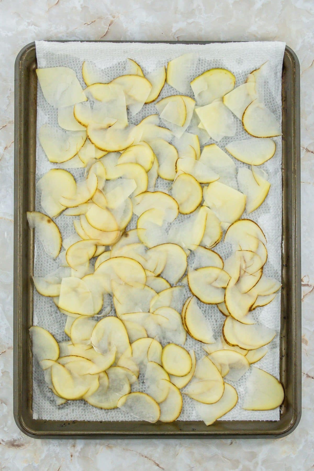 slices of raw potatoes on a parchment paper lined baking sheet