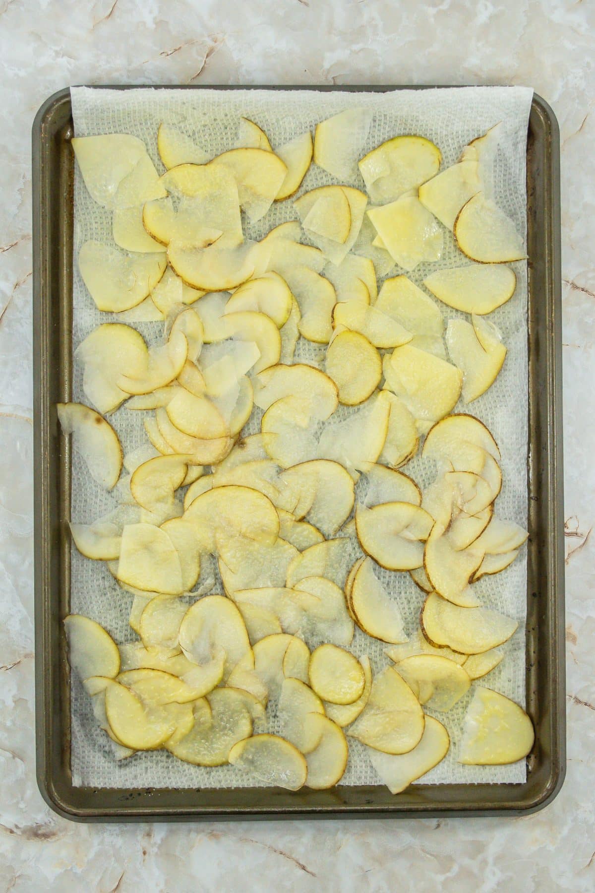slices of raw potato on a parchment lined baking sheet that have been patted dry