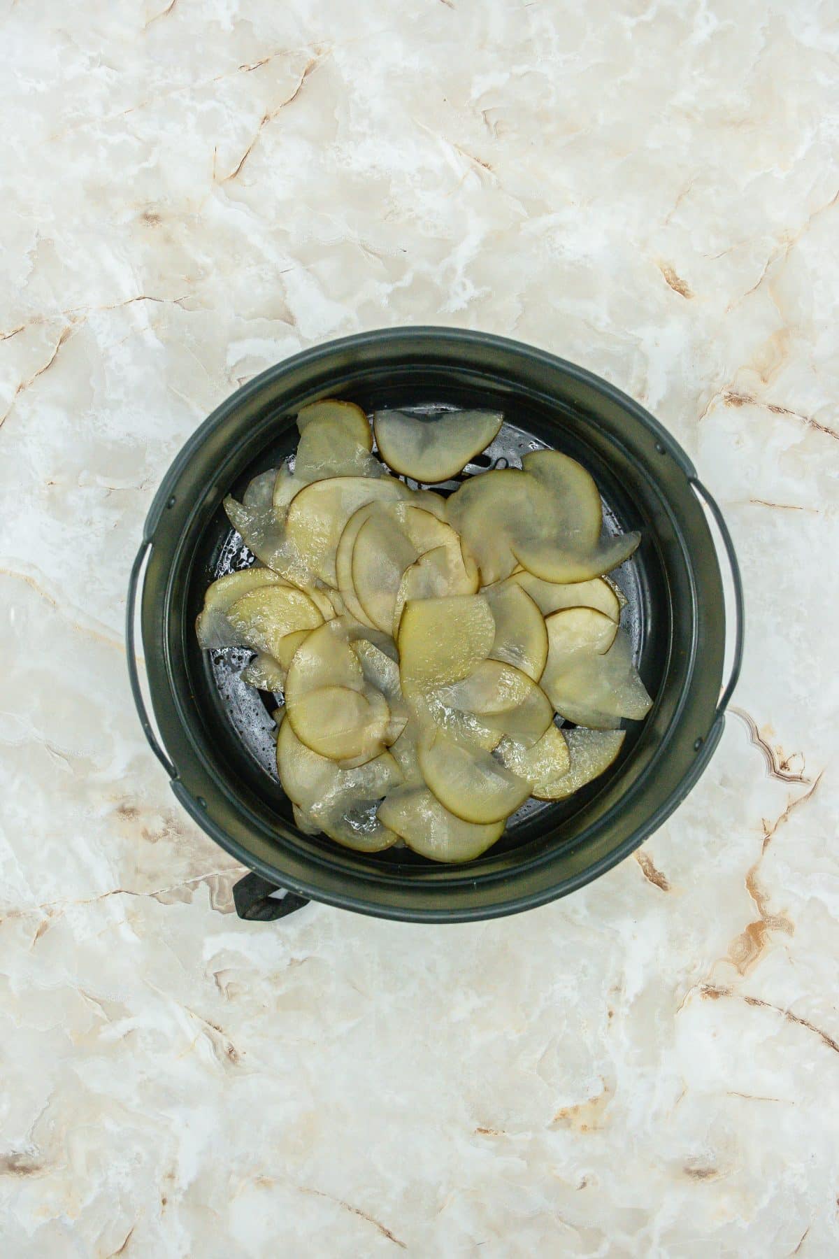slices of raw potato arranged in the basket of an air fryer