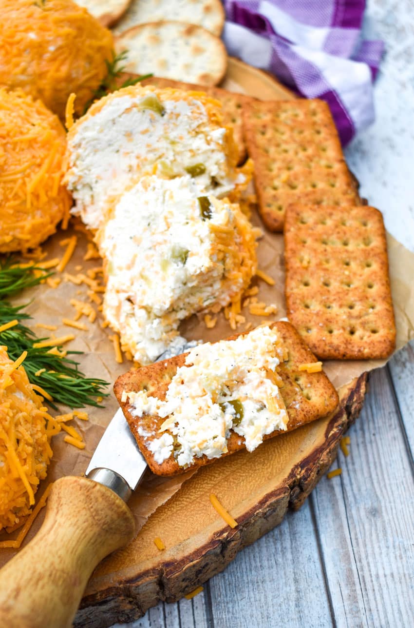 DILL PICKLE CREAM CHEESE SPREAD SPREAD ON A WHEAT CRACKER RESTING ON A WOODEN CUTTING BOARD